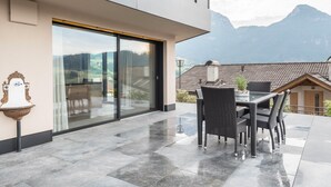 Un patio moderno al aire libre con una mesa y sillas de comedor, un gran ventanal corredera y vistas a las montañas.