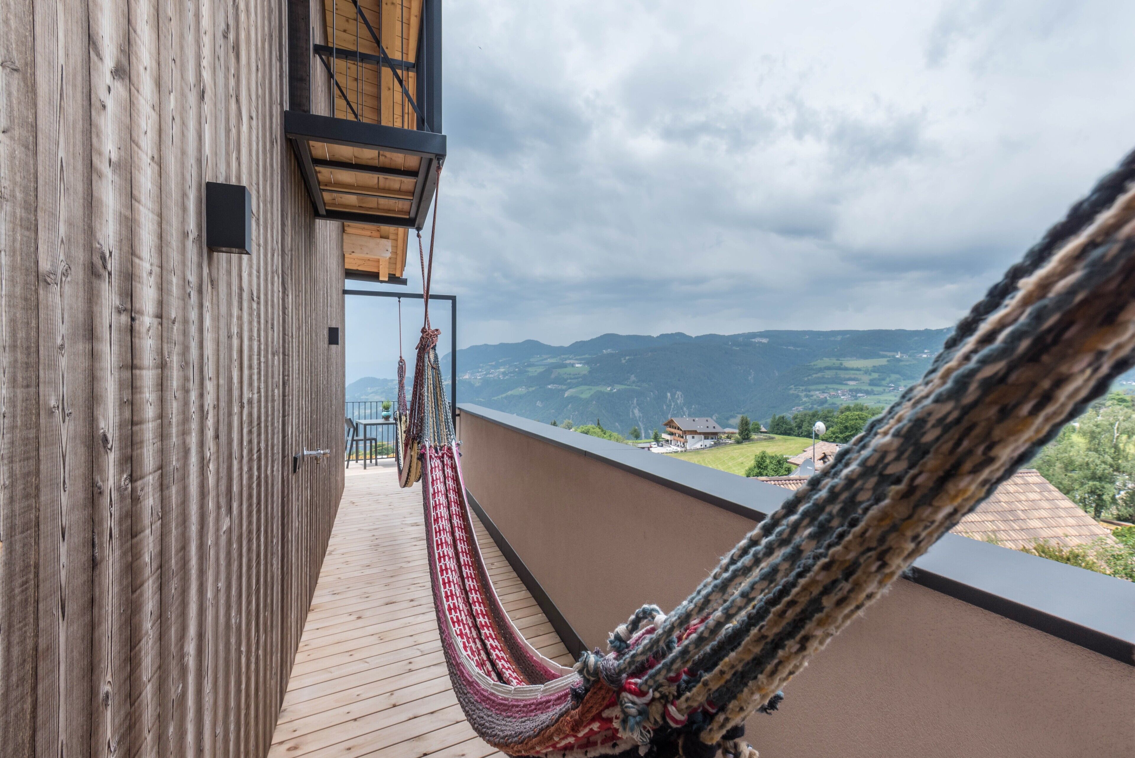 Un balcon en bois avec un hamac, offrant une vue sur un paysage montagneux.