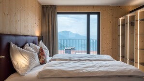 A hotel room with a large bed, wooden walls, a balcony with a view, and a wardrobe with illuminated shelves.