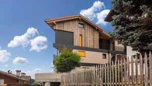 A modern two-story building with a stone wall and wooden fence, featuring a balcony and a small tree.