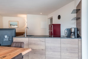 A modern kitchen with a wooden countertop, a red refrigerator, a coffee maker, and a dining area with a table and chairs.