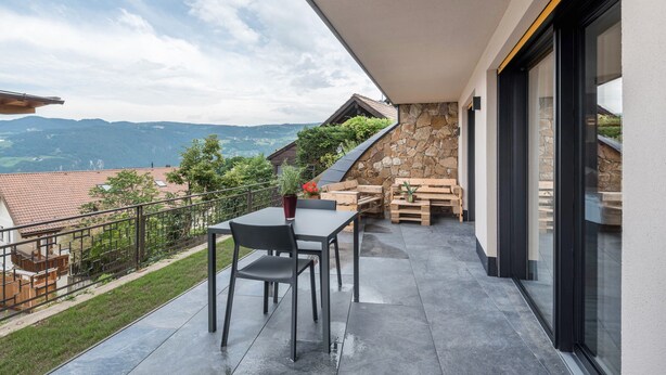 A balcony with a table and chairs, a stone wall, and a view of the countryside. - 'AUMIA Apartment Rubin' with Mountain View & terrace (Völs)