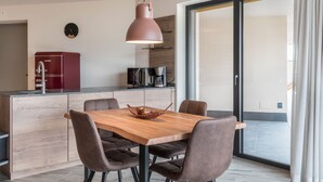 A modern kitchen with a wooden dining table, brown chairs, a hanging pendant light, and a red refrigerator. - 'AUMIA Apartment Rubin' with Mountain View & terrace (Völs)