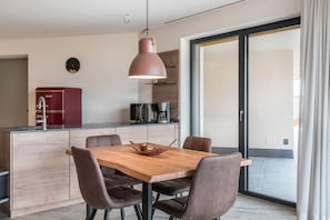 A modern kitchen with a wooden dining table, brown chairs, a hanging pendant light, and a red refrigerator.