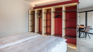 A bedroom with a bed, a red wardrobe with multiple shelves, and a dining area with a table and chairs. - 'AUMIA Apartment Rubin' with Mountain View & terrace (Völs)