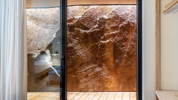 A room with a large rock wall, wooden flooring, and a sliding glass door.
