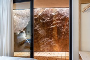 A room with a large rock wall, wooden flooring, and a sliding glass door.