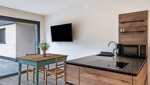 A modern kitchen with a wooden table, a built-in microwave, and a TV mounted on the wall.