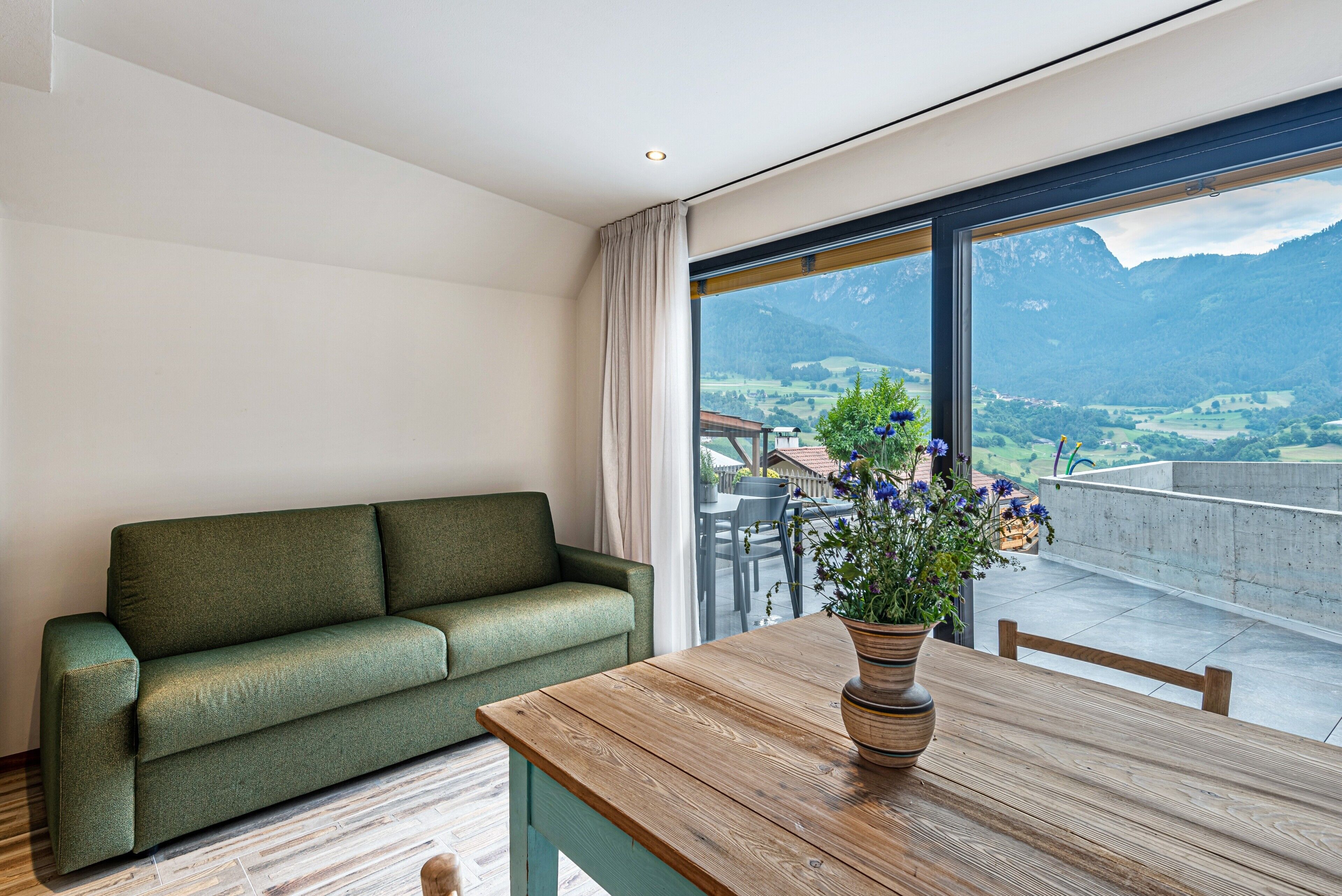 Una habitación con un sofá verde, una mesa de madera y un ventanal con vistas a la montaña.