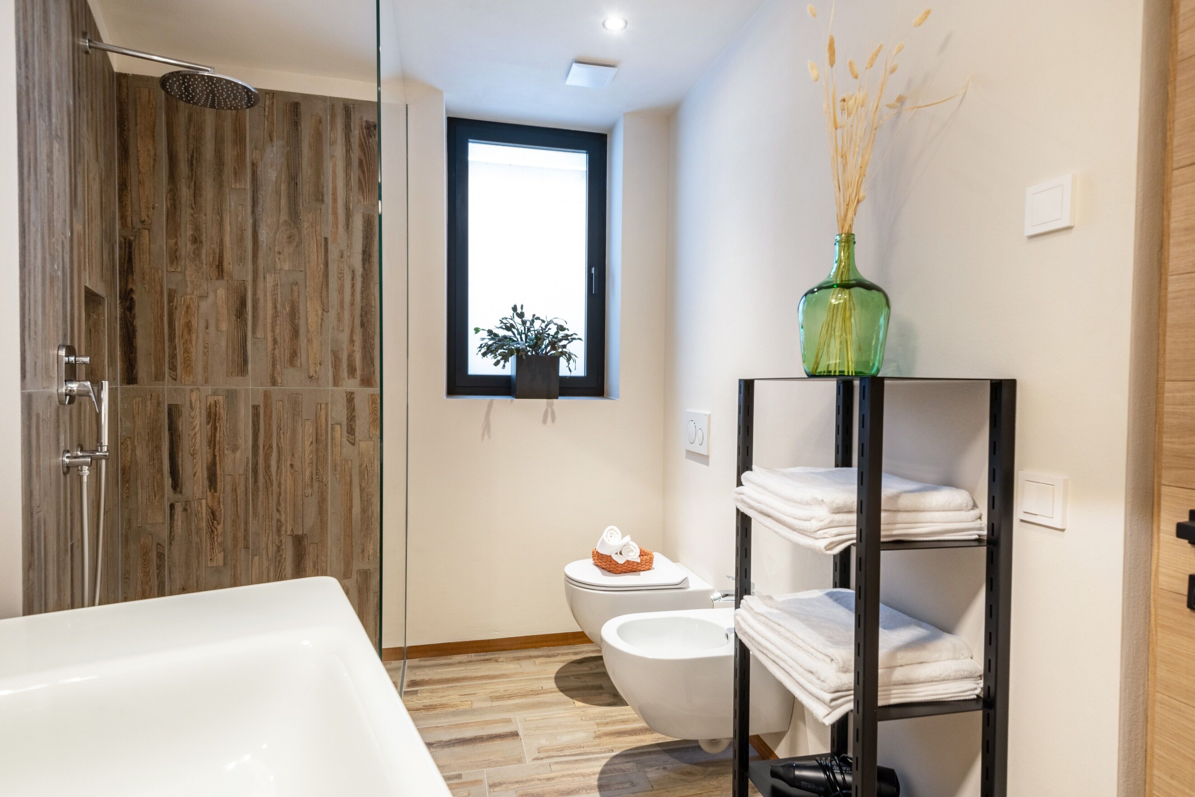 Une salle de bain moderne équipée d’une douche, de toilettes, d’un bidet et d’une étagère où sont rangées les serviettes.