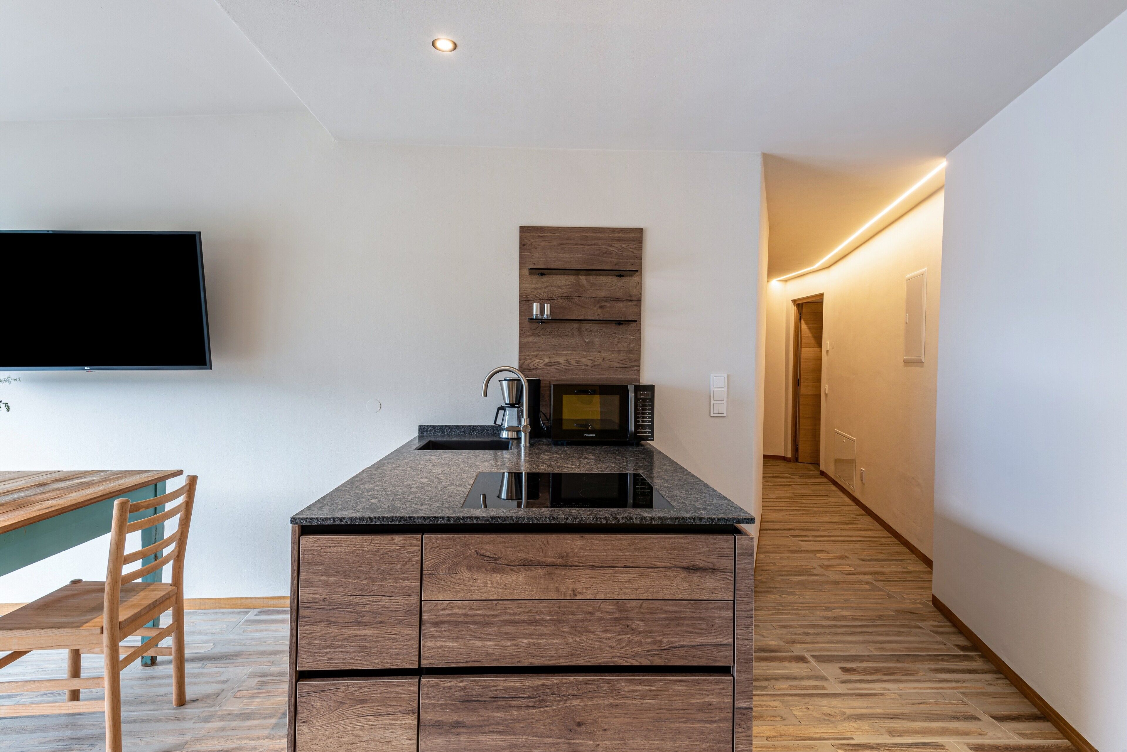 A modern kitchen with a built-in microwave, a flat-screen TV, and a wooden dining table.