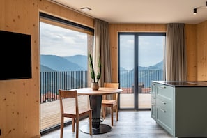 Una stanza moderna con arredamento in legno, un tavolo da pranzo con sedie, una zona cucina e un balcone con vista sulle montagne.