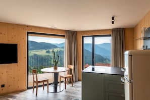Una stanza con balcone, un tavolo da pranzo, sedie, una TV e un angolo cottura.