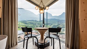 Ein Essbereich mit Tisch und Stühlen, einer Deckenleuchte und Blick auf eine Berglandschaft durch große Fenster.