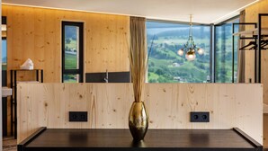 Ein modernes Zimmer mit einer Holzwand, einem schwarzen Tisch, einer goldenen Vase und Blick auf Grün durch große Fenster.