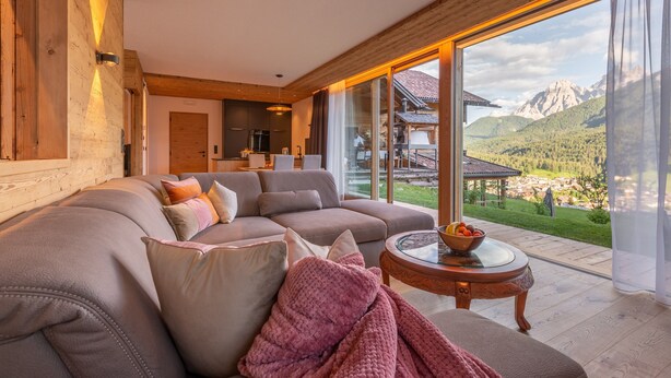 Una sala de estar moderna con un amplio sofá modular, una mesa de comedor de vidrio y vistas a las montañas.