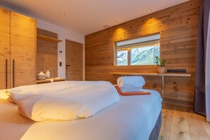 Ein modernes Schlafzimmer mit einem großen Bett, Holzwänden, einem Fenster mit Bergblick und einem Nachttisch mit Pflanze.