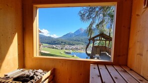 Una cabaña de madera con un ventanal grande que da a un paisaje montañoso, una estructura pequeña de madera y una chimenea.
