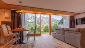 Una sala moderna con piso de madera, un sofá, una mesa de comedor con sillas y un ventanal con vistas a la montaña.