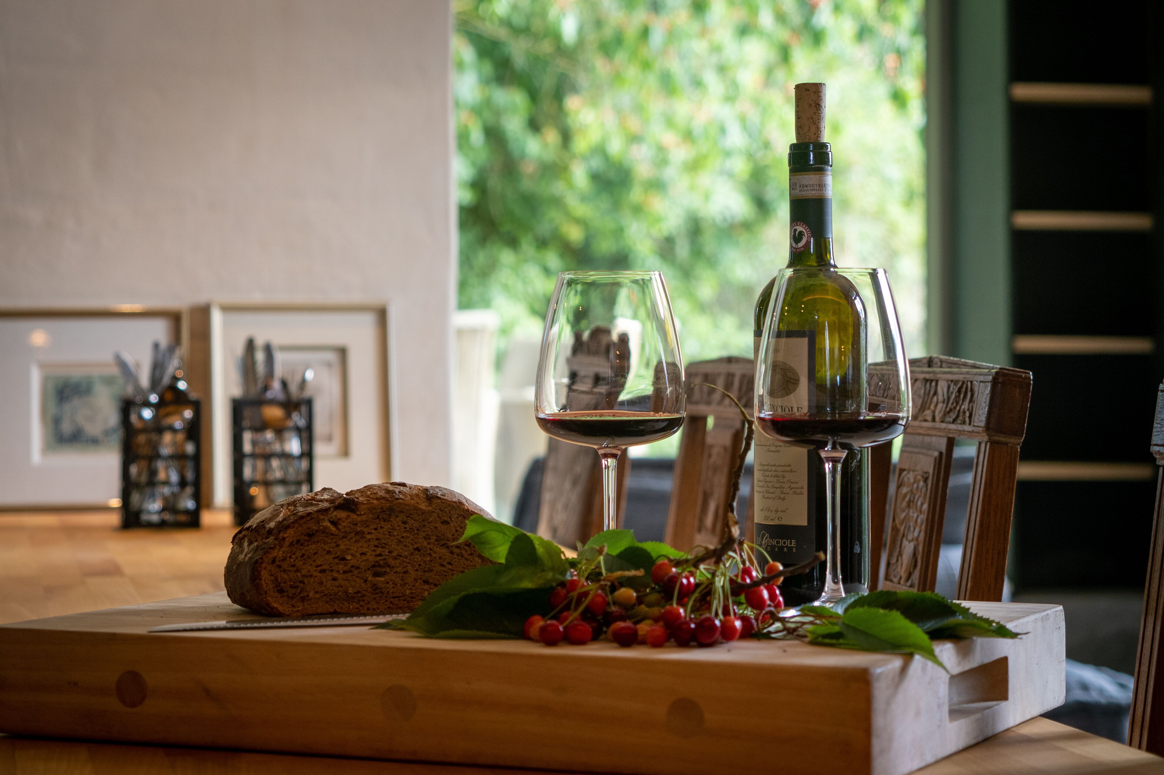 A wooden table with a loaf of bread, a bottle of wine, and two wine glasses.