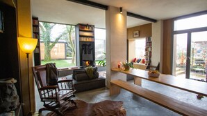 A modern living room with a fireplace, bookshelves, a dining table, and a view of the outdoors.