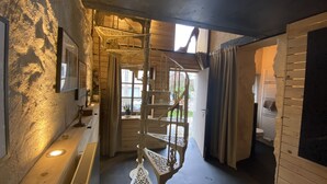 A rustic interior with a spiral staircase, wooden walls, and a window providing natural light.