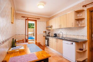 A kitchen with wooden cabinets, a dishwasher, and a dining table with placemats. - Villa Balena with Private Pool, Sea Views, Wi-Fi, and Air Conditioning (Sa Ràpita)