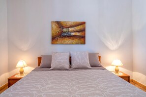 A neatly made bed with a patterned bedspread, two bedside lamps, and a single abstract painting on the wall.