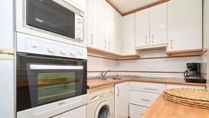 Una cocina compacta con microondas, horno, lavadora y encimera de madera.