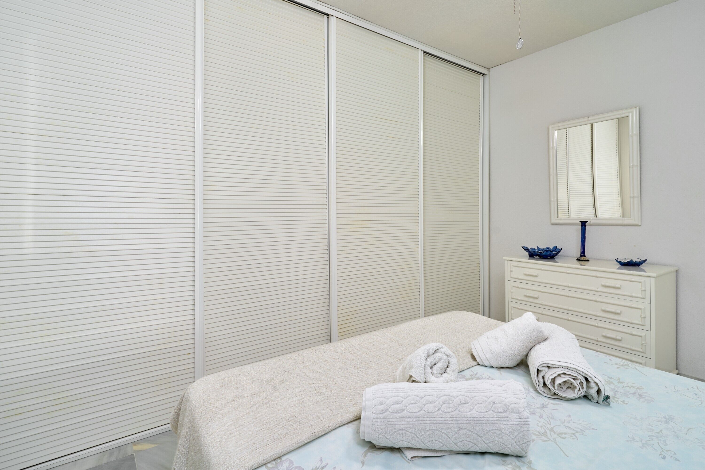 A bedroom with a bed, a dresser, a mirror, and a sliding door.