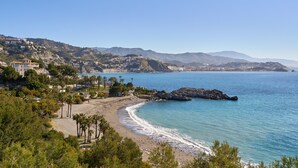 Un paisaje costero con una playa, afloramientos rocosos y un pueblo al fondo.