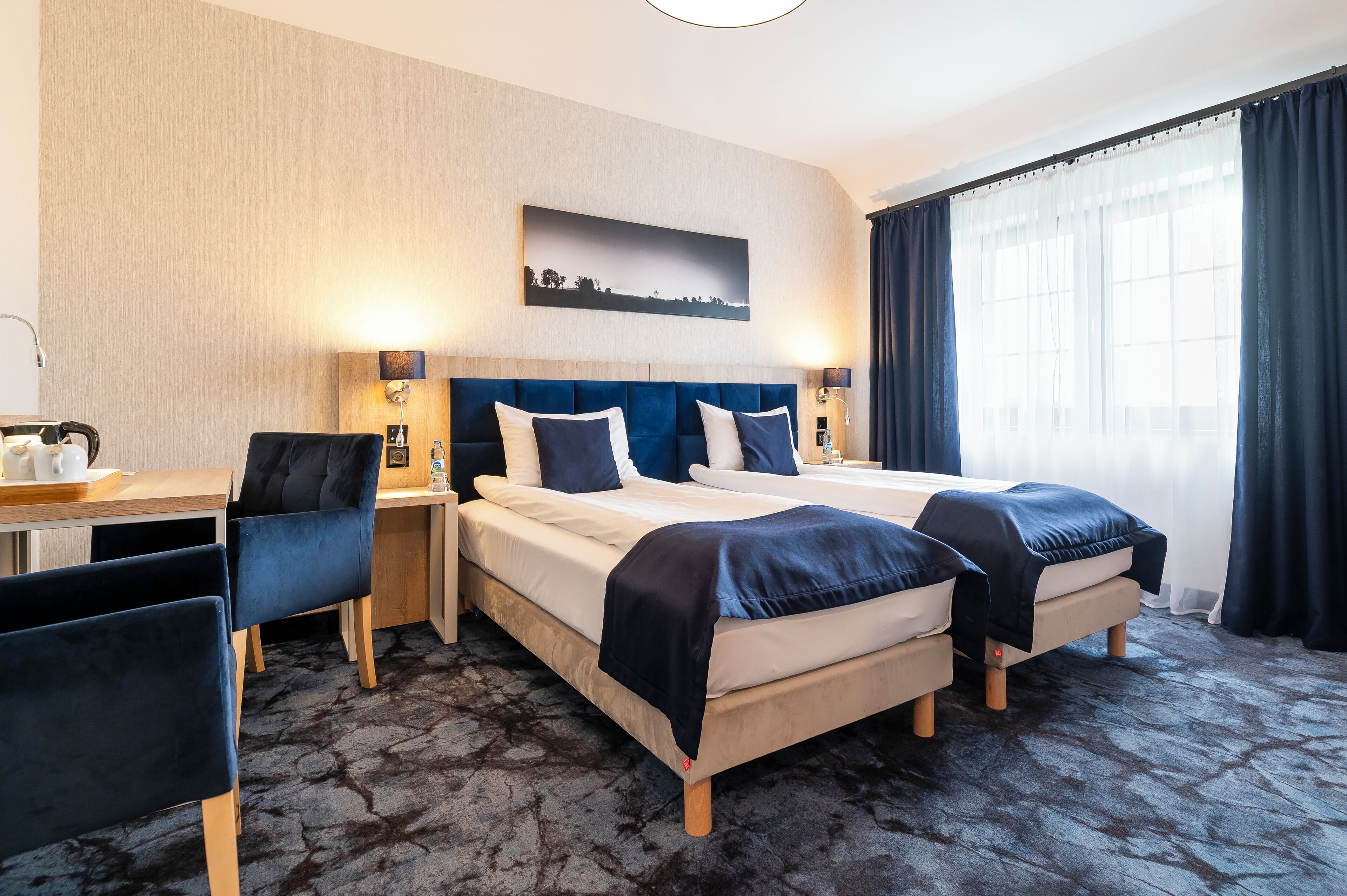 Een hotelkamer met twee bedden, een bureau, stoelen en een groot raam met gordijnen.