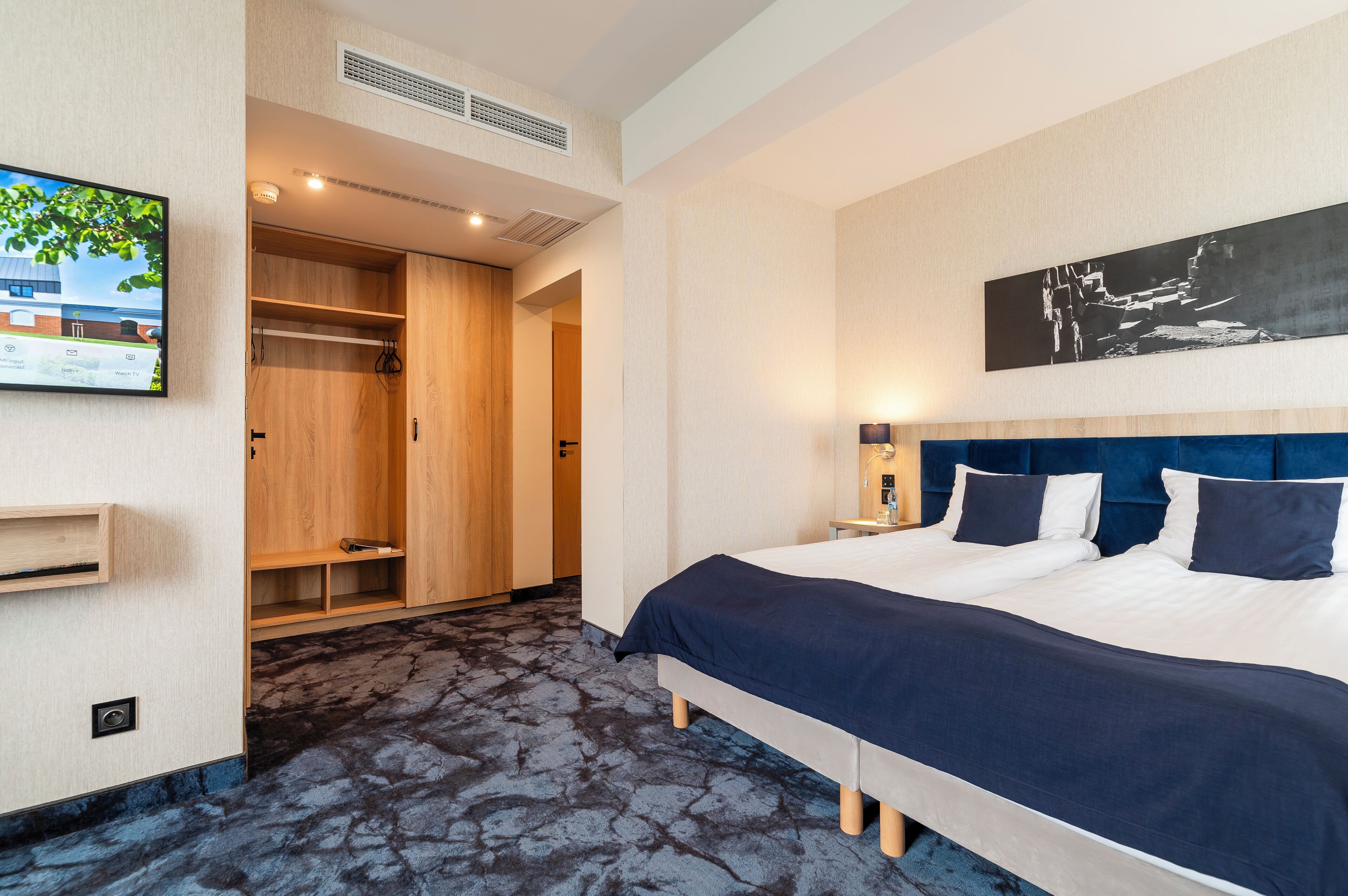 A hotel room with a bed, a wardrobe, a television, and a painting on the wall.