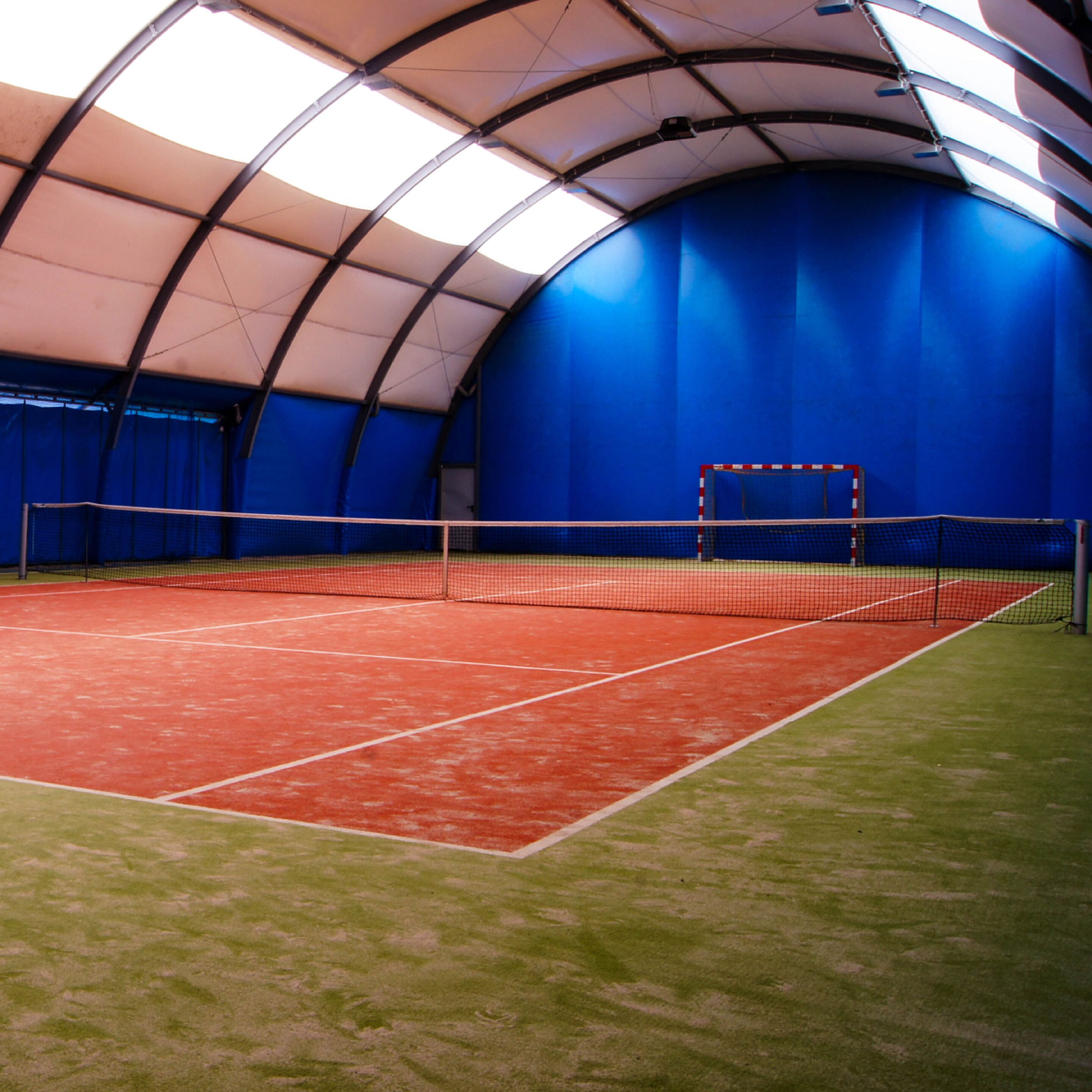An indoor tennis court with a net, blue walls, and a red playing surface.