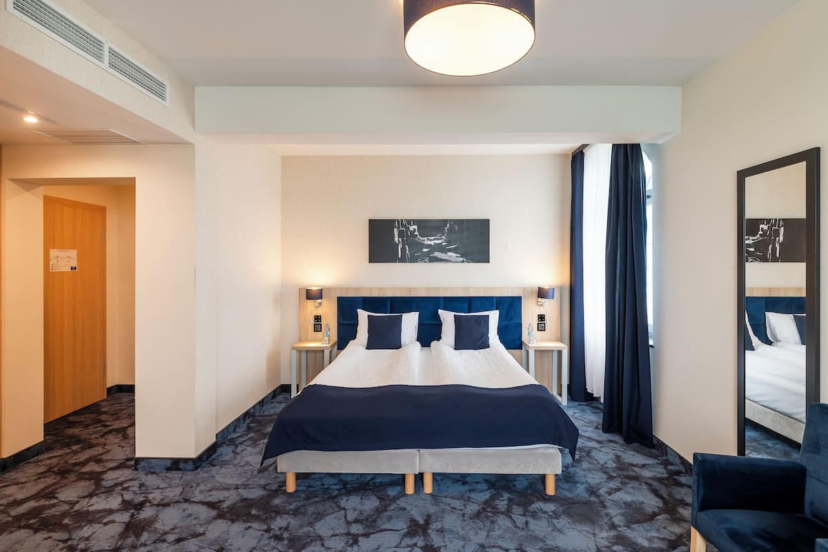 Een hotelkamer met een groot bed, nachtkastjes, een hoofdbord, een plafondlamp, een schilderij aan de muur en een spiegel.