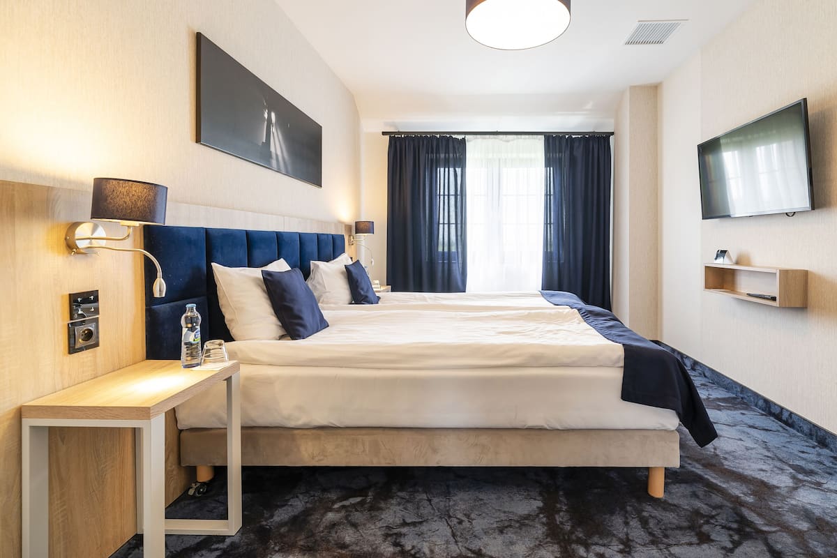 Een hotelkamer met een groot bed, nachtkastjes, een flatscreen televisie en een raam met gordijnen.