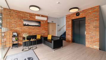 A modern lobby with brick walls, a reception desk, two sofas, and a staircase.