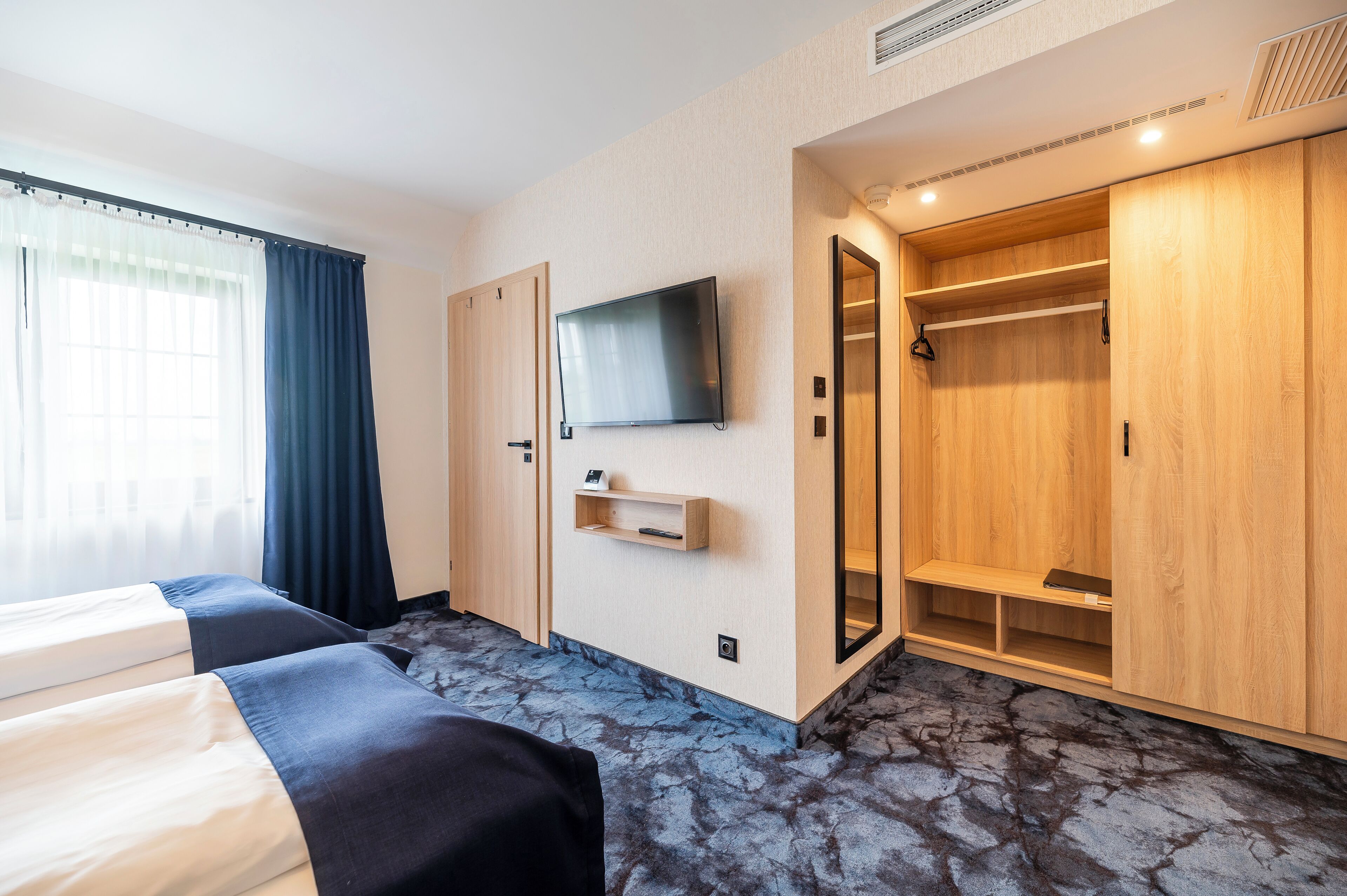 A hotel room with a bed, a TV mounted on the wall, a wardrobe, and a mirror.