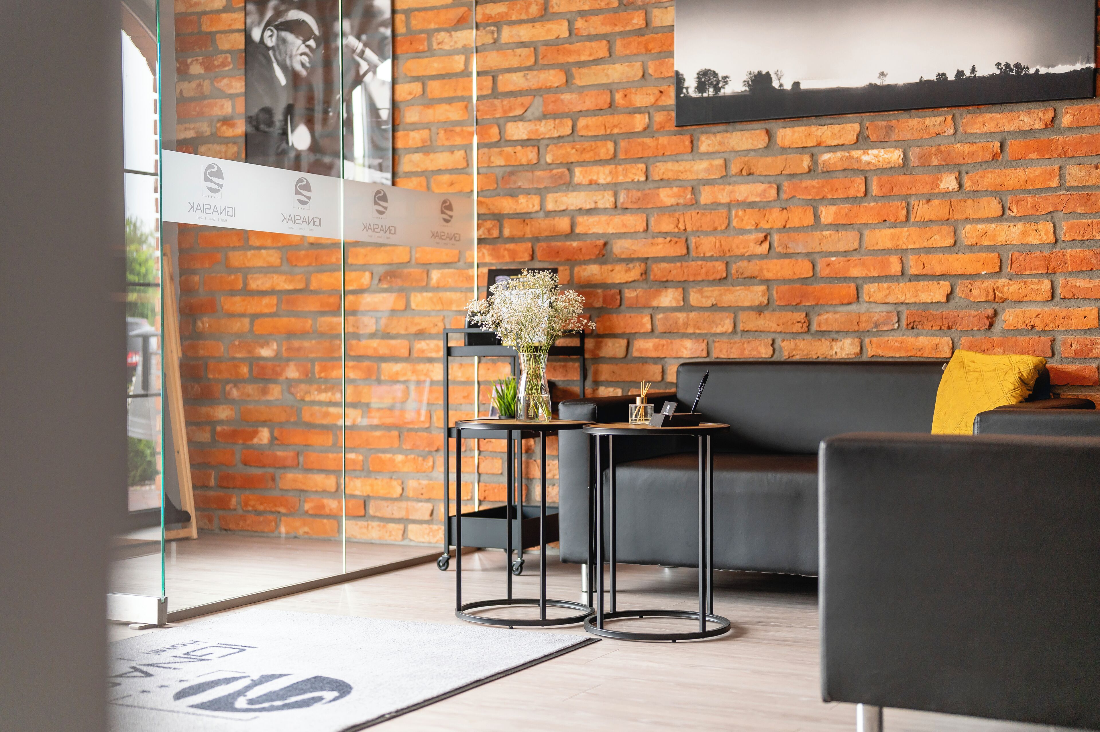 Une pièce moderne avec un mur en briques, un canapé noir, une petite table avec un vase et un fauteuil noir.