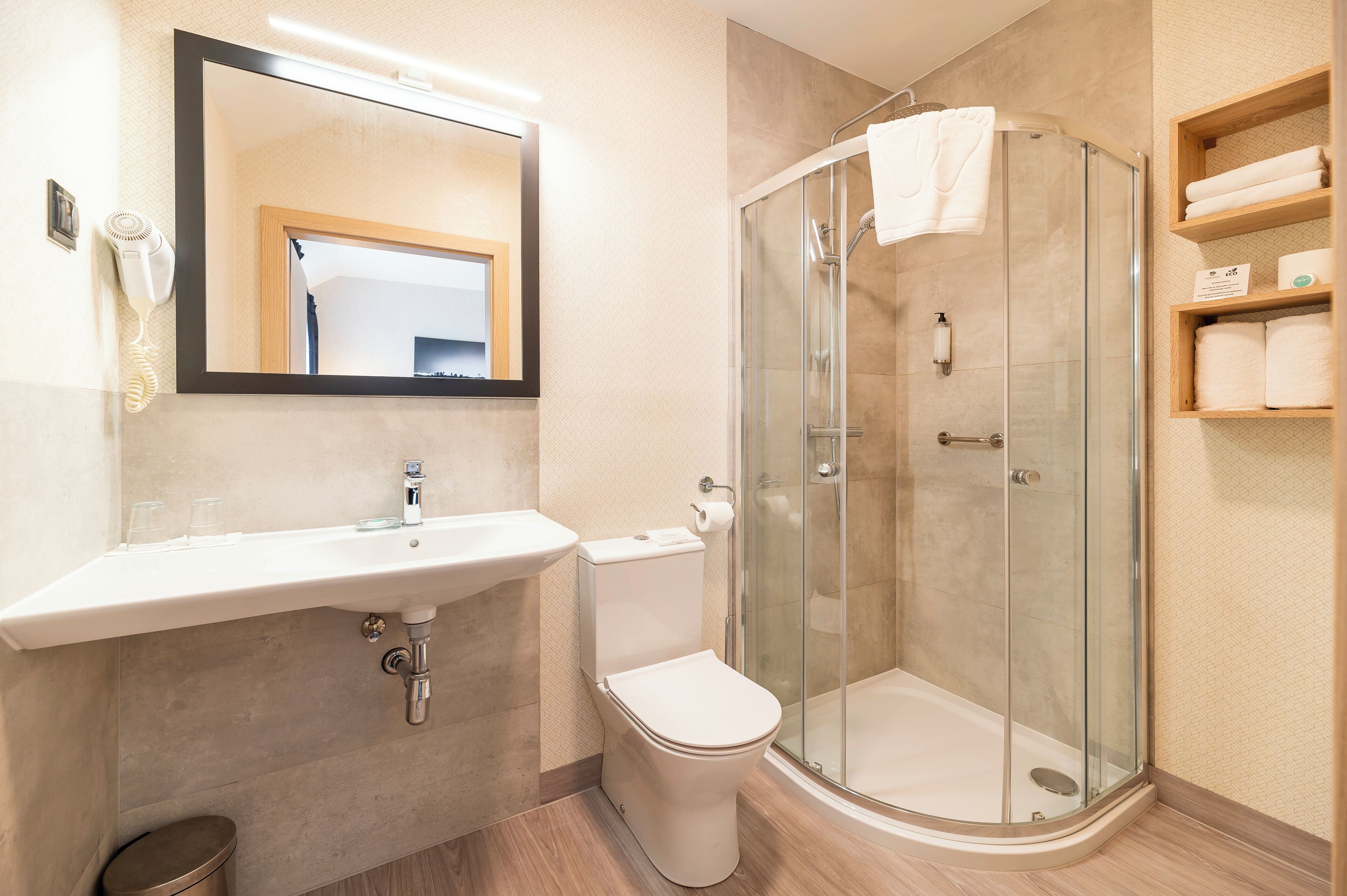 A modern bathroom with a glass-enclosed shower, a sink with a mirror above, and a toilet.