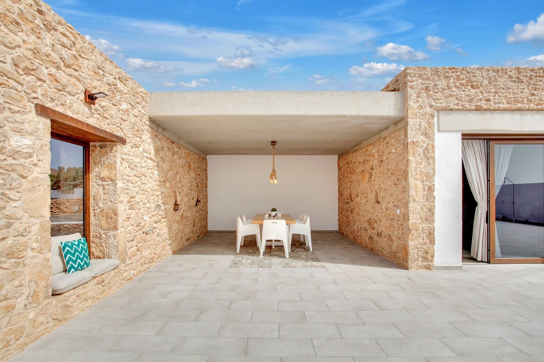 Una habitación con paredes de piedra, una mesa de comedor y sillas, una lámpara colgante y vistas a través de una ventana.