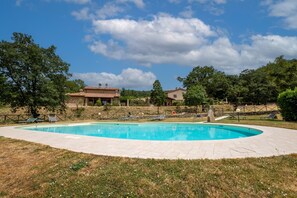 A swimming pool with lounge chairs, a fenced area, and a house in the background.