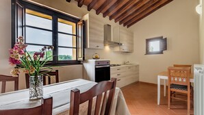 Een keuken met houten kastjes, een eettafel met stoelen en een raam met uitzicht.
