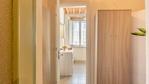 Un couloir menant à une salle de bain équipée d’une armoire en bois, d’un lavabo et d’une fenêtre avec des rideaux.