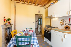 Une cuisine équipée d’une cuisinière à gaz, de meubles blancs et d’une nappe à carreaux.
