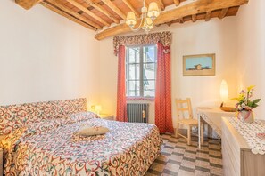 Une chambre à coucher avec un lit, une fenêtre avec des rideaux, une table avec une lampe et une chaise.