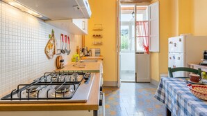 Une cuisine équipée d’une cuisinière à gaz, d’un plan de travail carrelé de carreaux blancs, d’un plafond en bois et offrant une vue sur l’extérieur grâce à une porte ouverte.