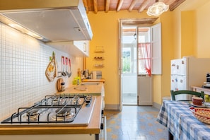 Cocina con estufa a gas, salpicadero de azulejos blancos, techo de madera y vista a través de una puerta abierta.