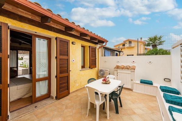 Un patio con tavolo e sedie, una porta scorrevole in vetro e un muro bianco con decorazioni.