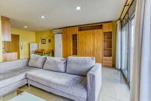 Un salon avec un canapé gris, des meubles en bois et une porte vitrée donnant sur un balcon.